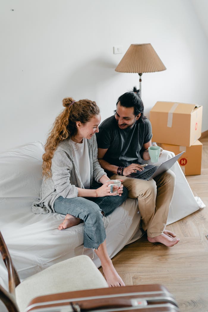 services-01 Joyful couple using a laptop and coffee in their new apartment, surrounded by moving boxes.
